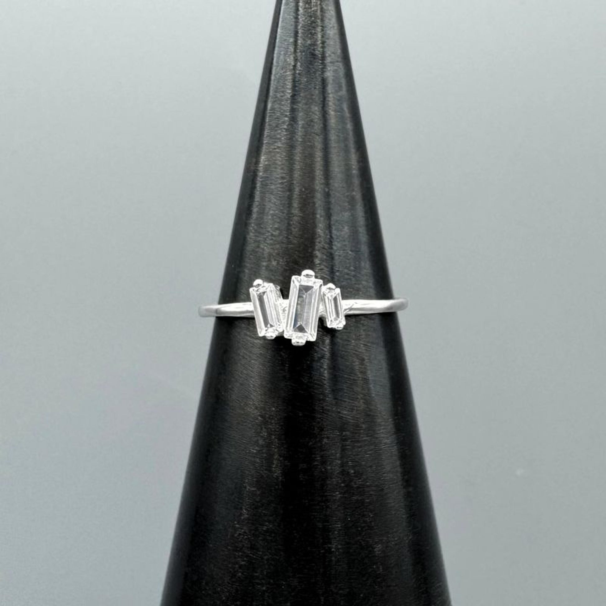 Silver ring with baguette-cut gemstones on a black stand against a gray background