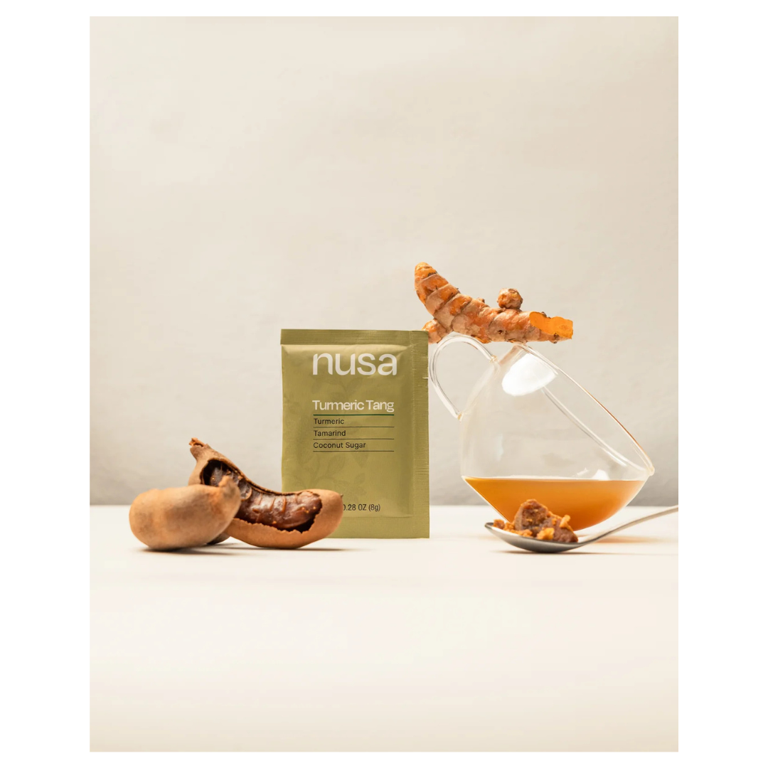 Nusa Tumeric Tang package with tumeric root and a glass filled with the drink.