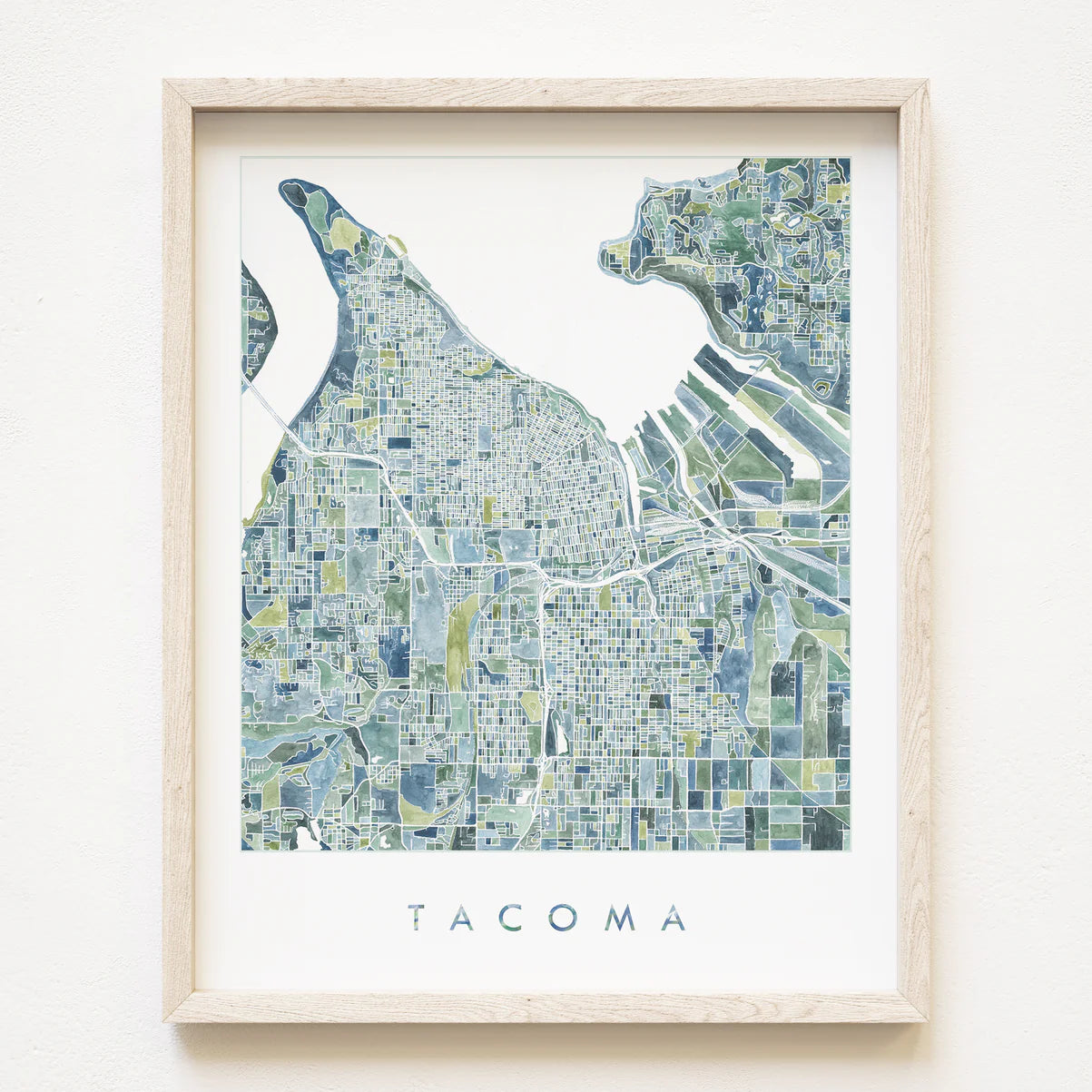 Framed map of Tacoma with a light wood frame on a white wall. The item for sale does not include a frame.
