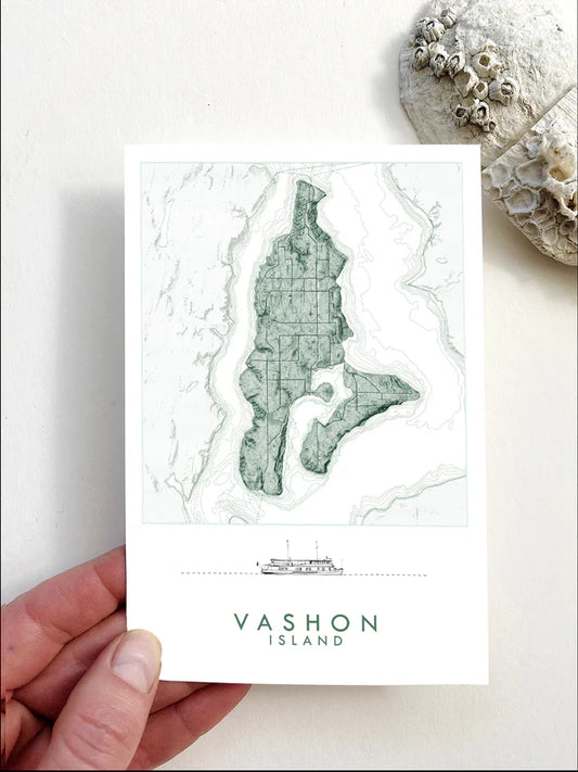Postcard of a map of Vashon Island held by a hand with a stone and shell in the background