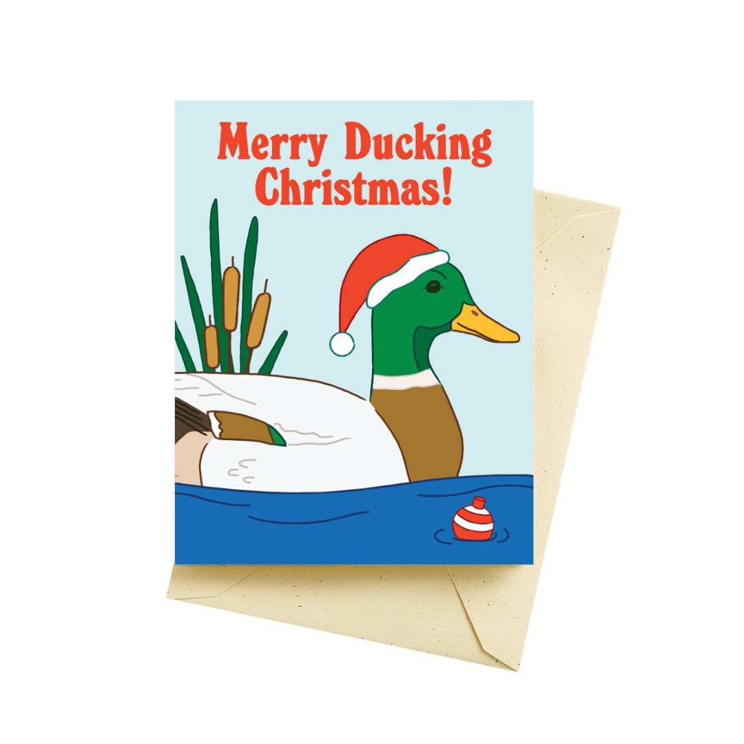 Baby blue holiday card with a green and brown duck floating in the water next to a red and white buoy with the words "Merry Ducking Christmas!" in a red font. Pictured with a tan colored envelope.