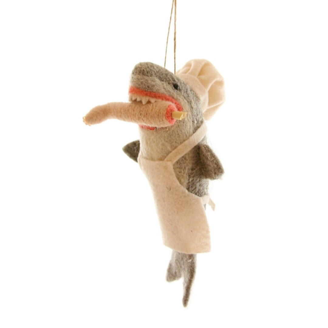Felted shark dressed in a chef's hat and white apron with a human leg in its shark-y mouth.