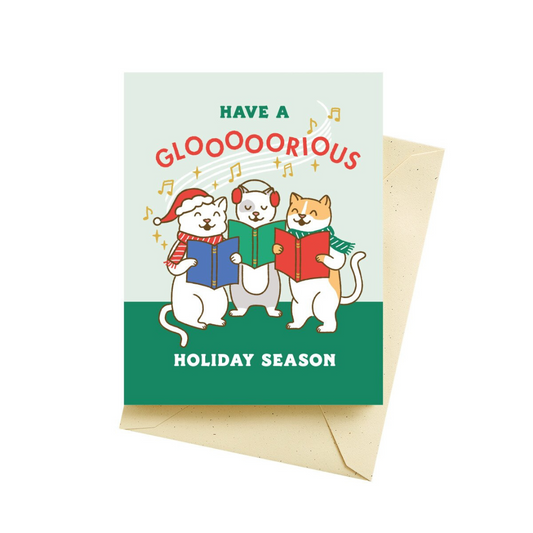 Aquamarine and wintergreen colored holiday card featuring three singing cats dressed in holiday attire white holding sheet music. Gold musical notes floating above them with the words "Have a glooooorious holiday season". Pictured with a tan colored envelope.