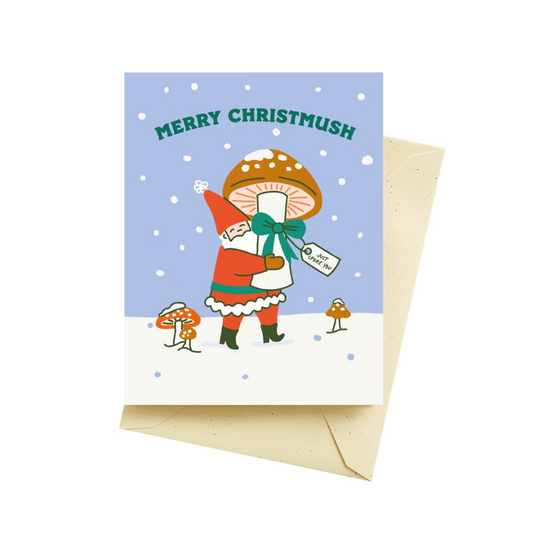 Holiday greeting card featuring Santa dressed in red, walking through the snow carrying a brown mushroom wrapped in a green bow with a gift tag that reads "just spore you". Behind Santa is a blue sky with falling snowflakes and the words "Merry Christmush" in green. Pictured with a tan colored envelope,