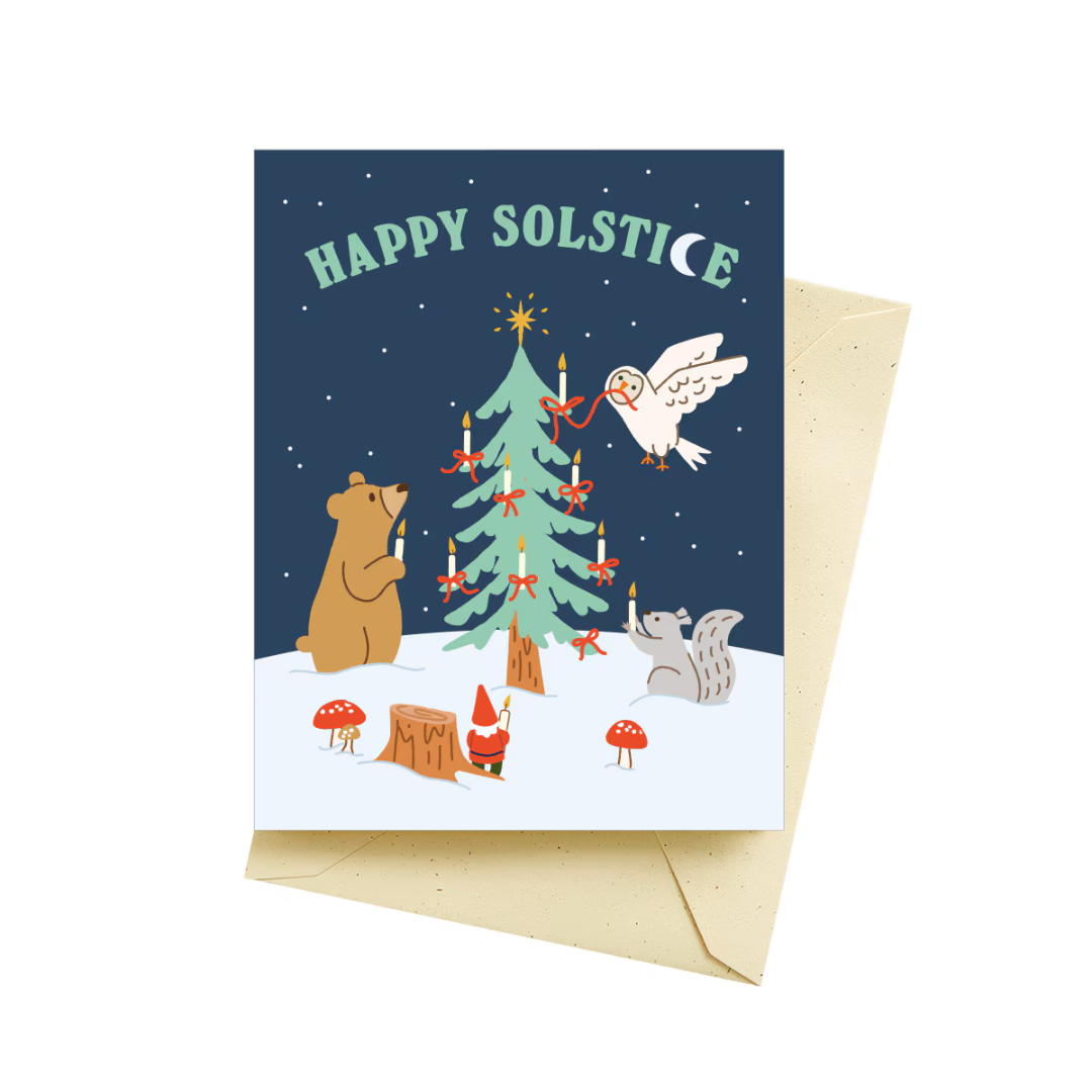 Holiday card featuring a navy blue night sky covered in stars and a decorated Christmas tree in the snow surrounded by a brown bear, white turtle dove, gray squirrel and a gnome dressed in red, all admiring the tree. The words "happy solstice" appear in green with a white crescent shaped moon for the letter C in solstice. Pictured with a tan colored envelope.