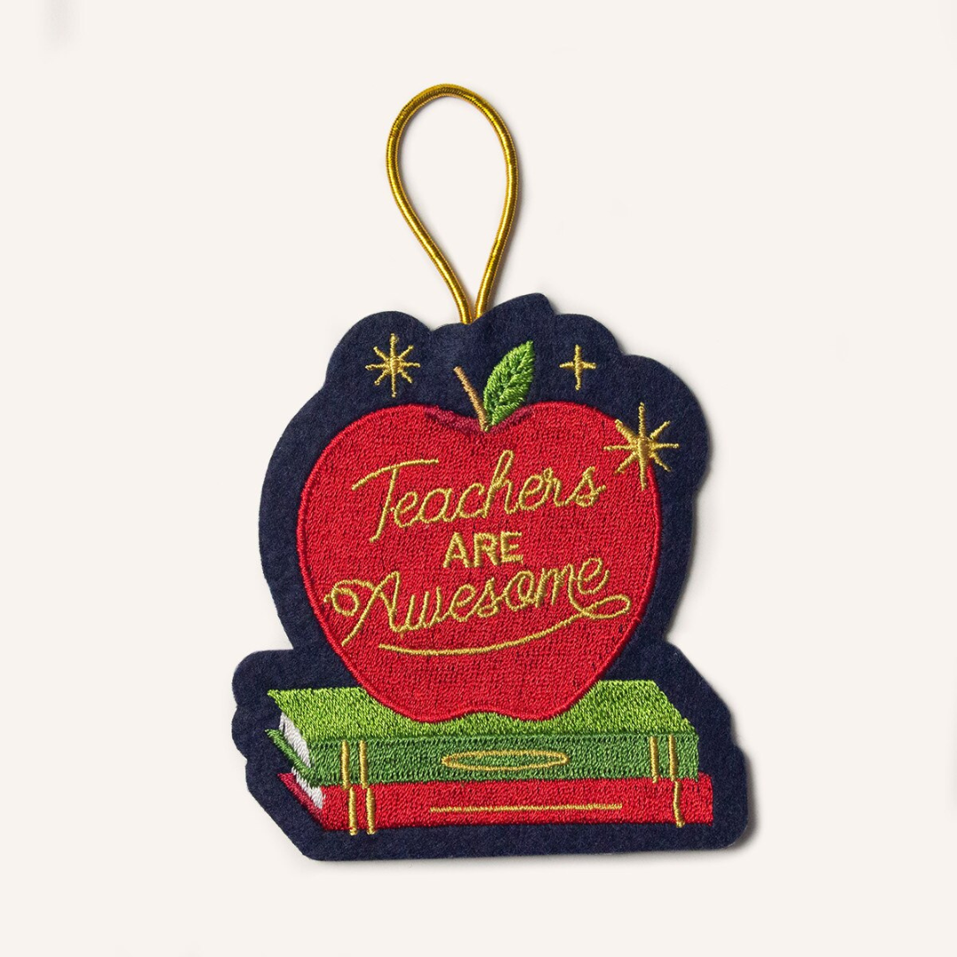 Navy blue felt ornament  hung by gold cord featuring a red apple sitting on top of red and green books with the words "teachers are awesome" across it in gold lettering.