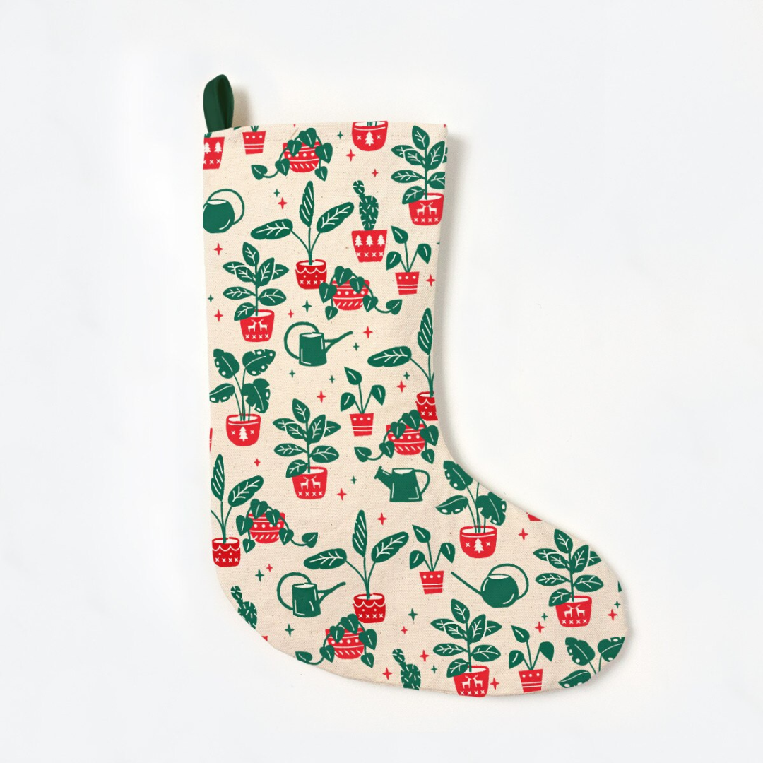 Creamy white stocking featuring a green hook to hang, with a red and green pattern of plants and watering cans.