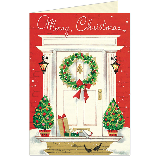 Greeting card featuring a red home at Christmastime with a white front doorstep and on it, a green wreath tied with a red bow, gold hardware, two tiny trees decorated with lights and ornaments and a few wrapped gifts at the foot of the door. The words "Merry Christmas" in white  are above.