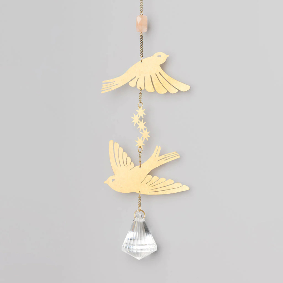 Gold suncatcher featuring a pink gem at the top and two birds in the middle, with an opaque sunstone at the bottom.