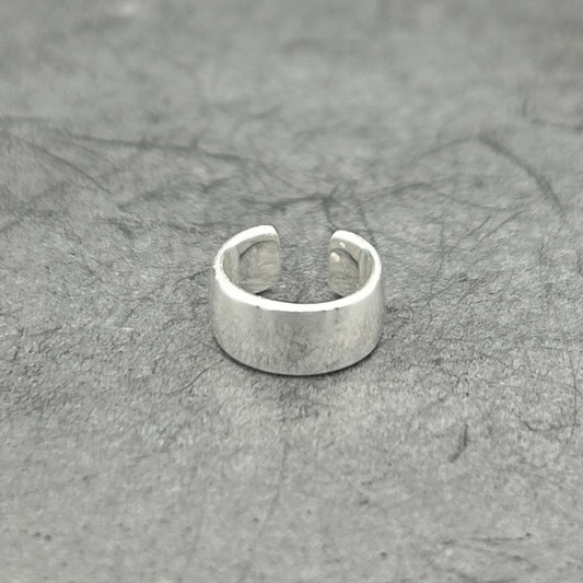 Wide silver ear cuff sitting atop of a gray surface.