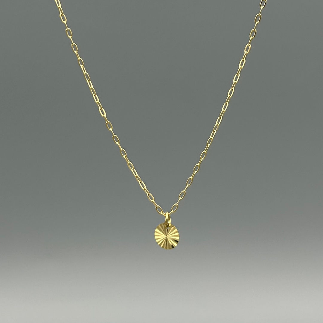 Gold chained necklace with a gold disc pendant featuring a beveled design that looks like sun rays.