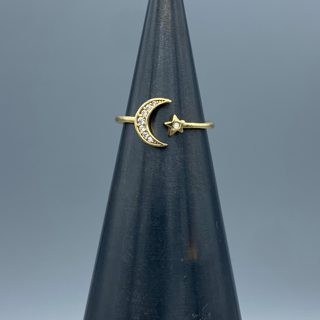 Gold ring featuring a gold band and a cubic zirconium filled moon on one side and a star on the other side of the band, joining together to form the ring.