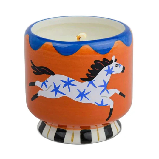 Candle in a decorative container with a horse design on an orange background