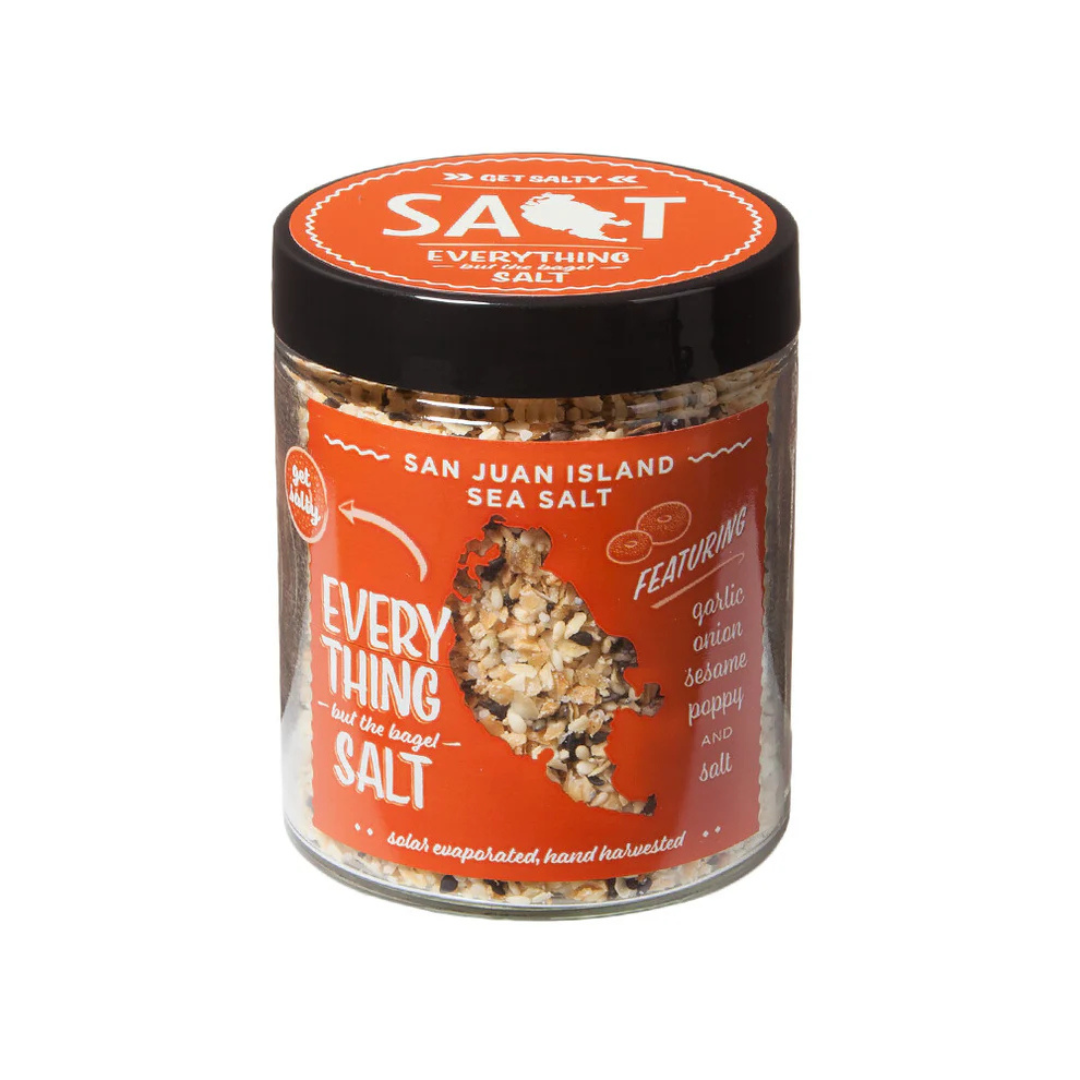 Glass jar of seasoning blend with a black lid and a tomato red label on the front with the San Juan Island Sea Salt brand name and "everything but the bagel salt" flavor in white lettering.