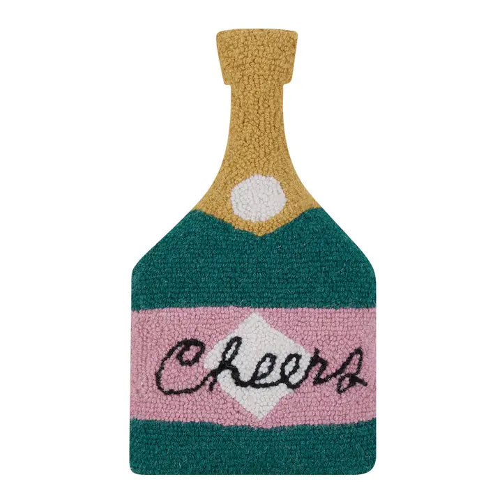 Bottle shaped green accent pillow with a gold top and pink label that says "Cheers"