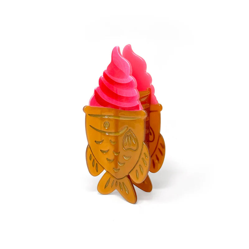 Hair claw clip in the shape of pink soft serve ice cream in a fish shaped cookie cone.