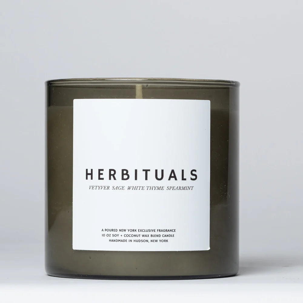 Herbituals candle with a white square label on a smokey taupe glass container