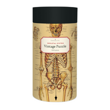 Load image into Gallery viewer, Cavallini round puzzle box with a navy lid and cream case, adorned with a vintage skeletal system illustration, with anatomical and physiological labelling..
